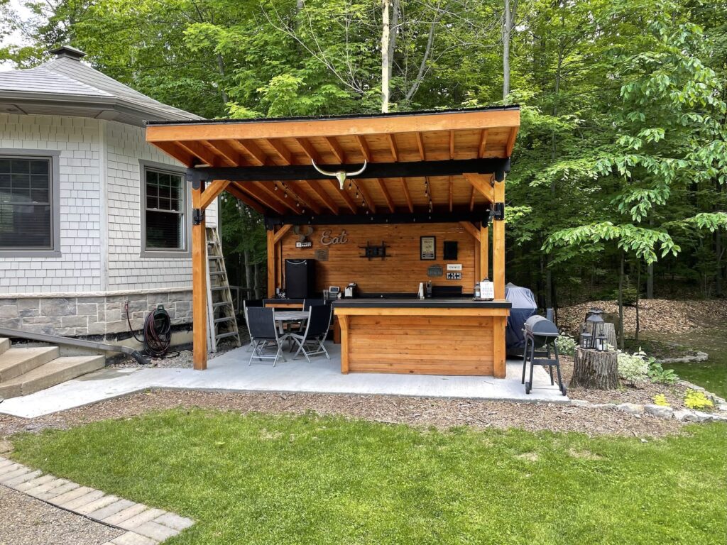 Une cuisine extérieure couverte avec comptoir et bar en bois — pour les longues soirées d'été.