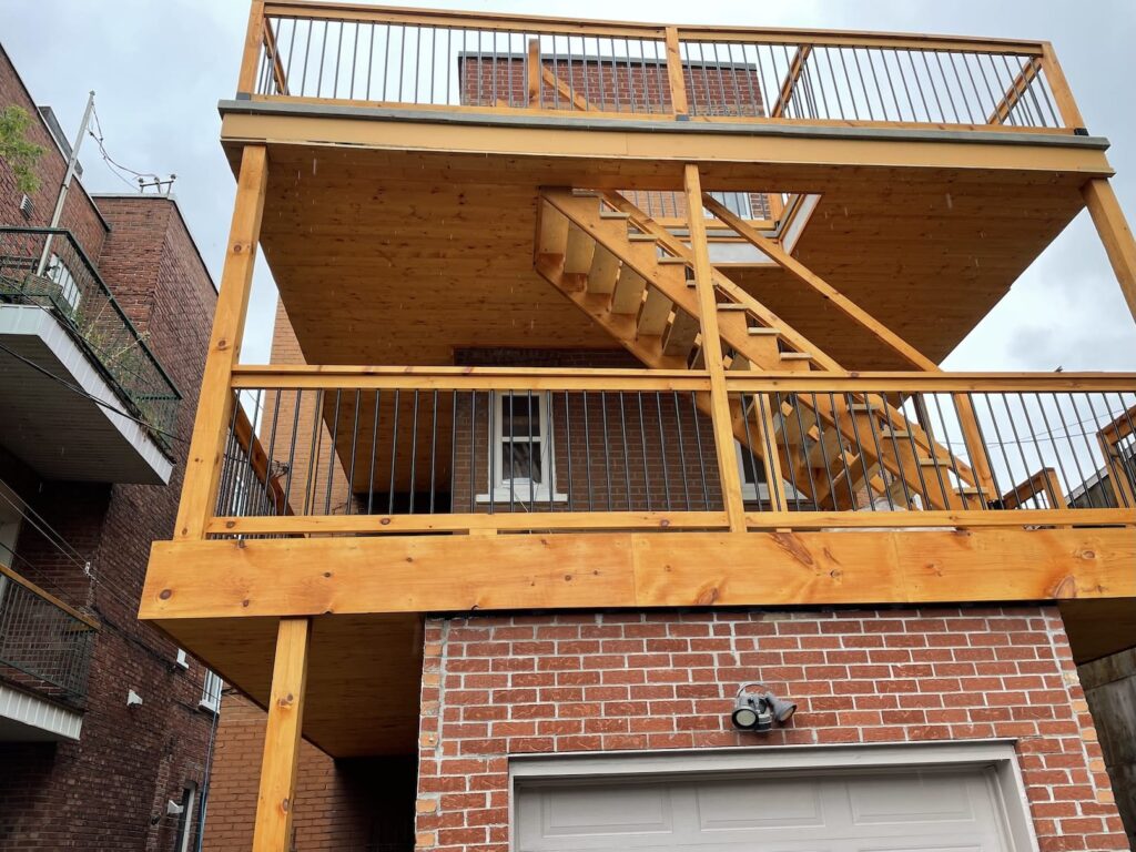 Un balcon sur deux niveaux sur un immeuble en brique — nouvelle structure, plancher et garde-corps.
